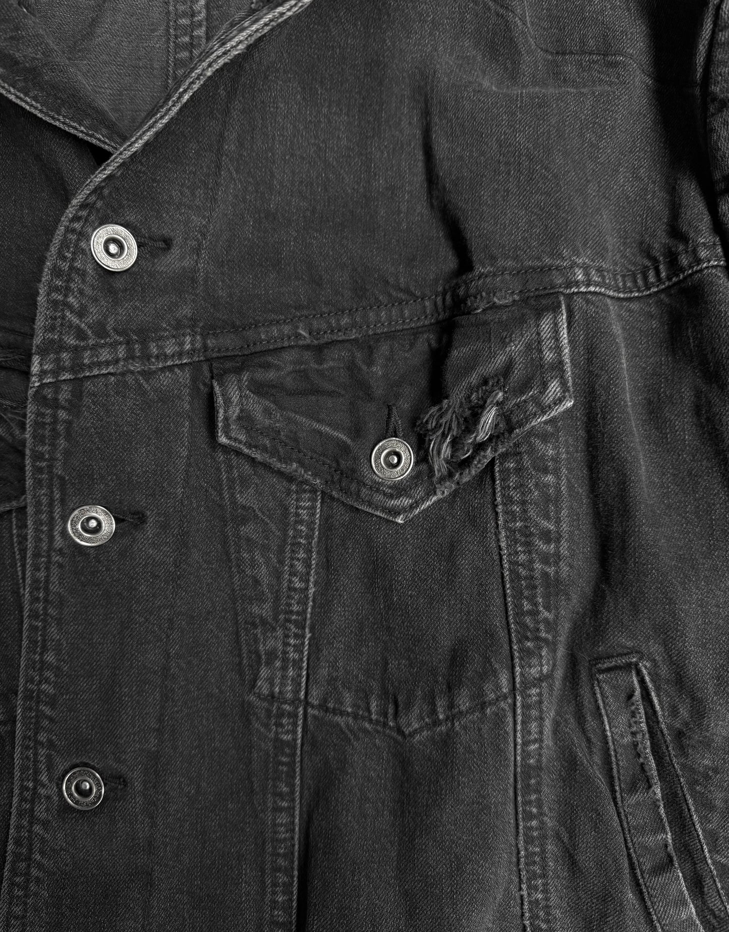 Close-up of a dark denim jacket with buttons and a pocket.