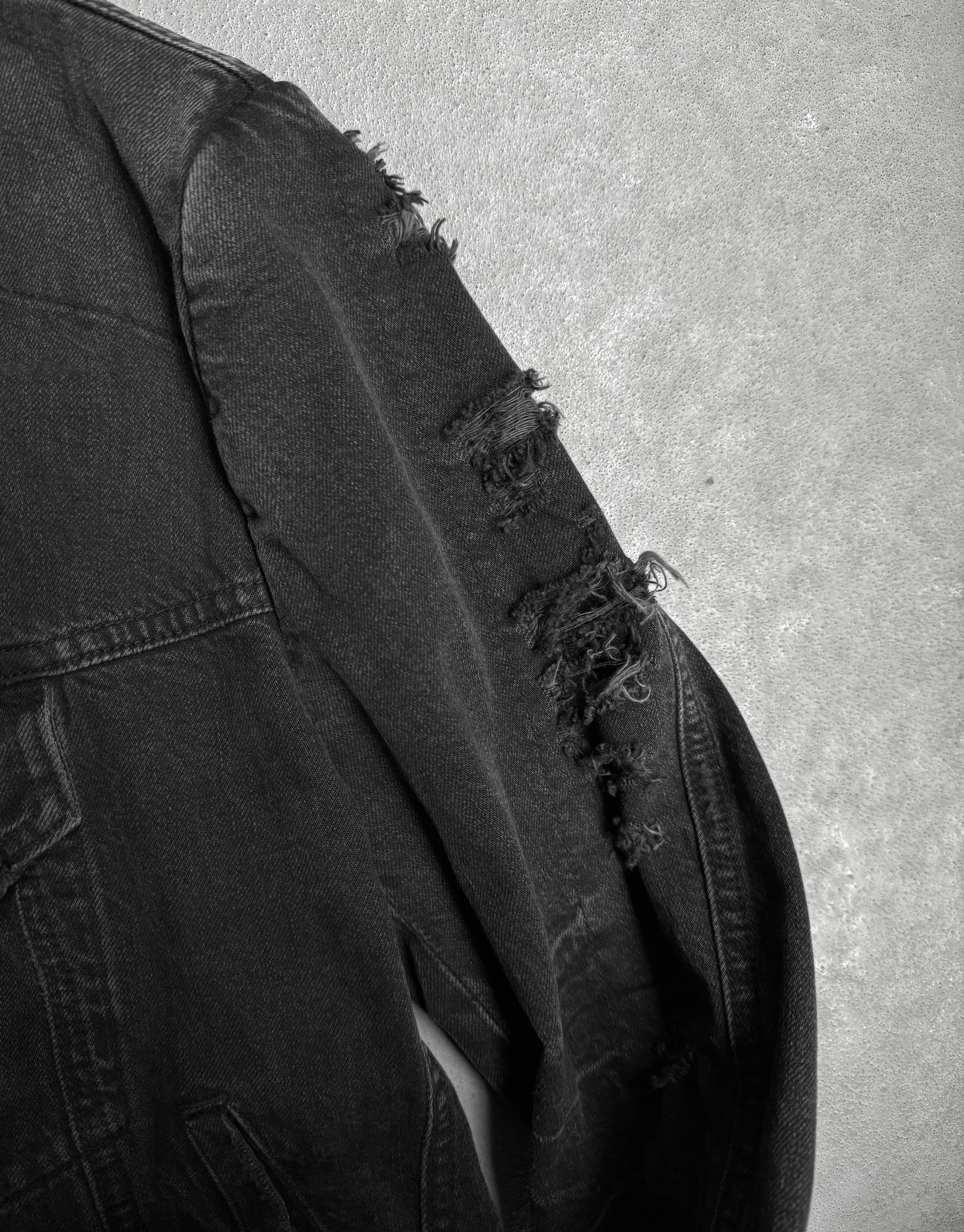 Black denim jacket with distressed details on a gray background