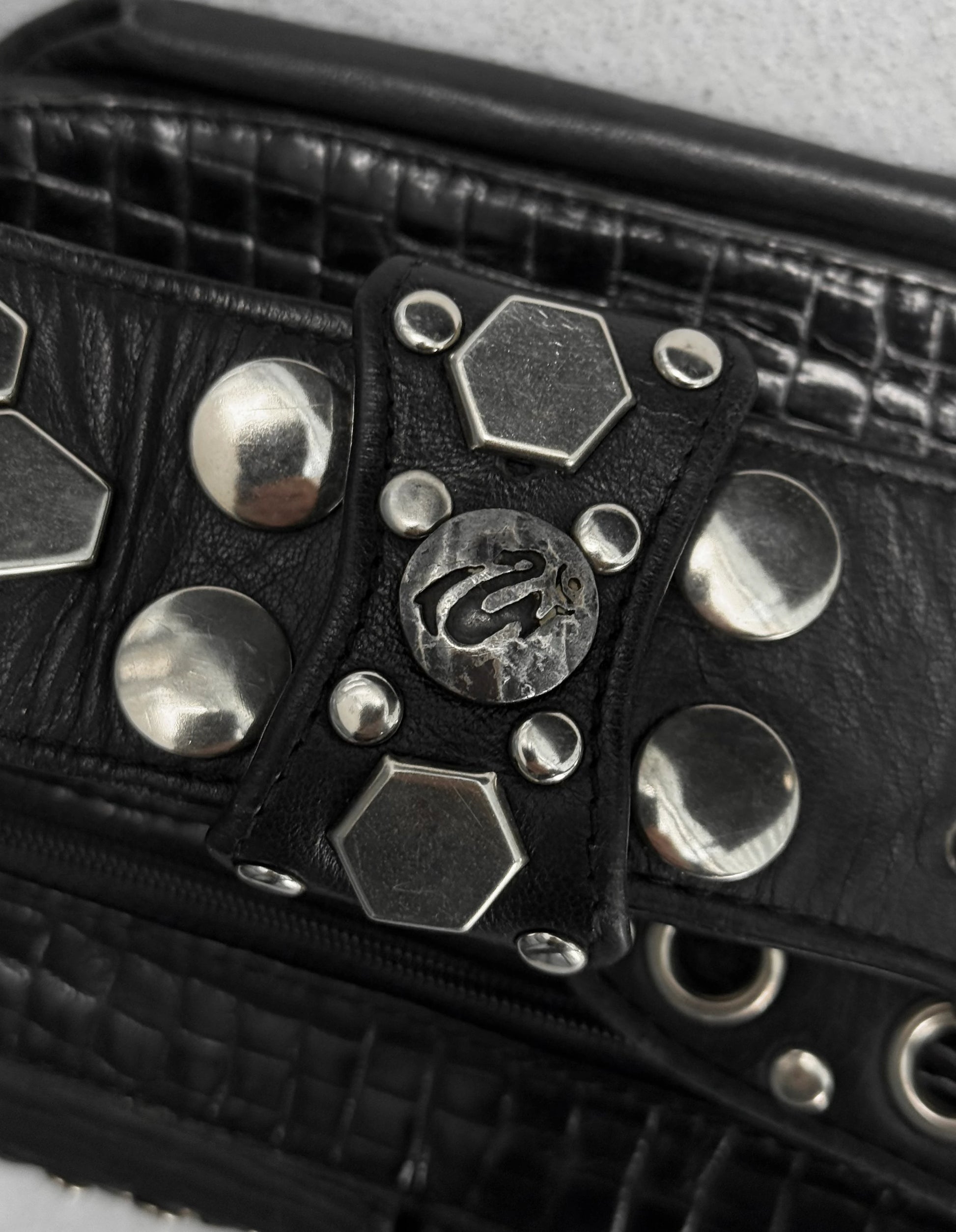 Black leather bag with silver studs and a brand logo on a light gray background