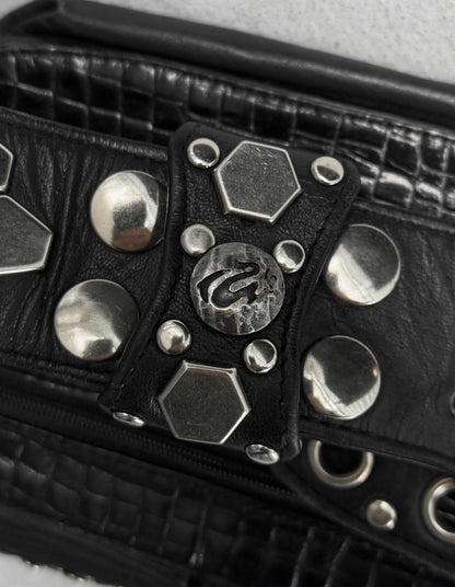 Black leather bag with silver studs and a brand logo on a light gray background