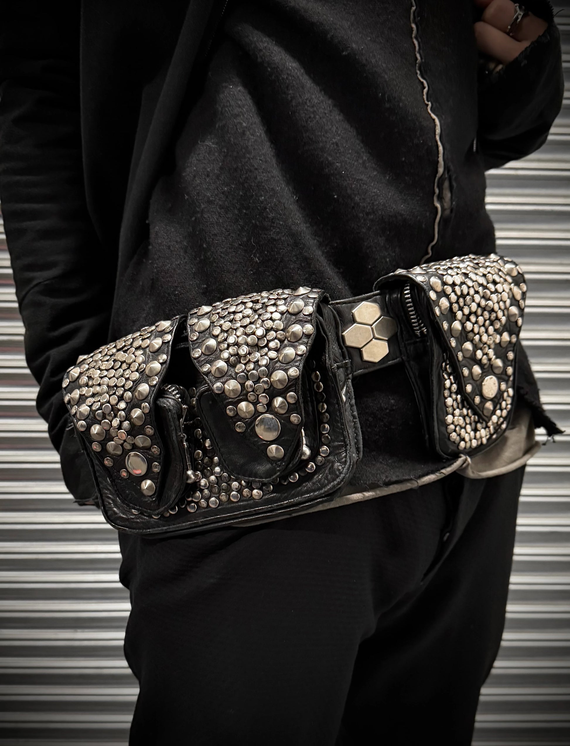 Black studded belt worn by a person against a striped background