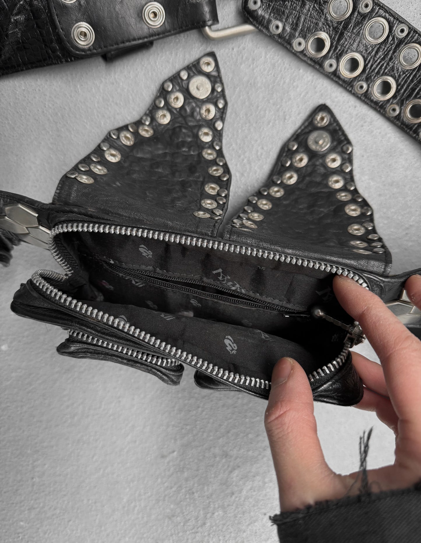 Black studded wallet with triangular design held open by a hand on a gray background