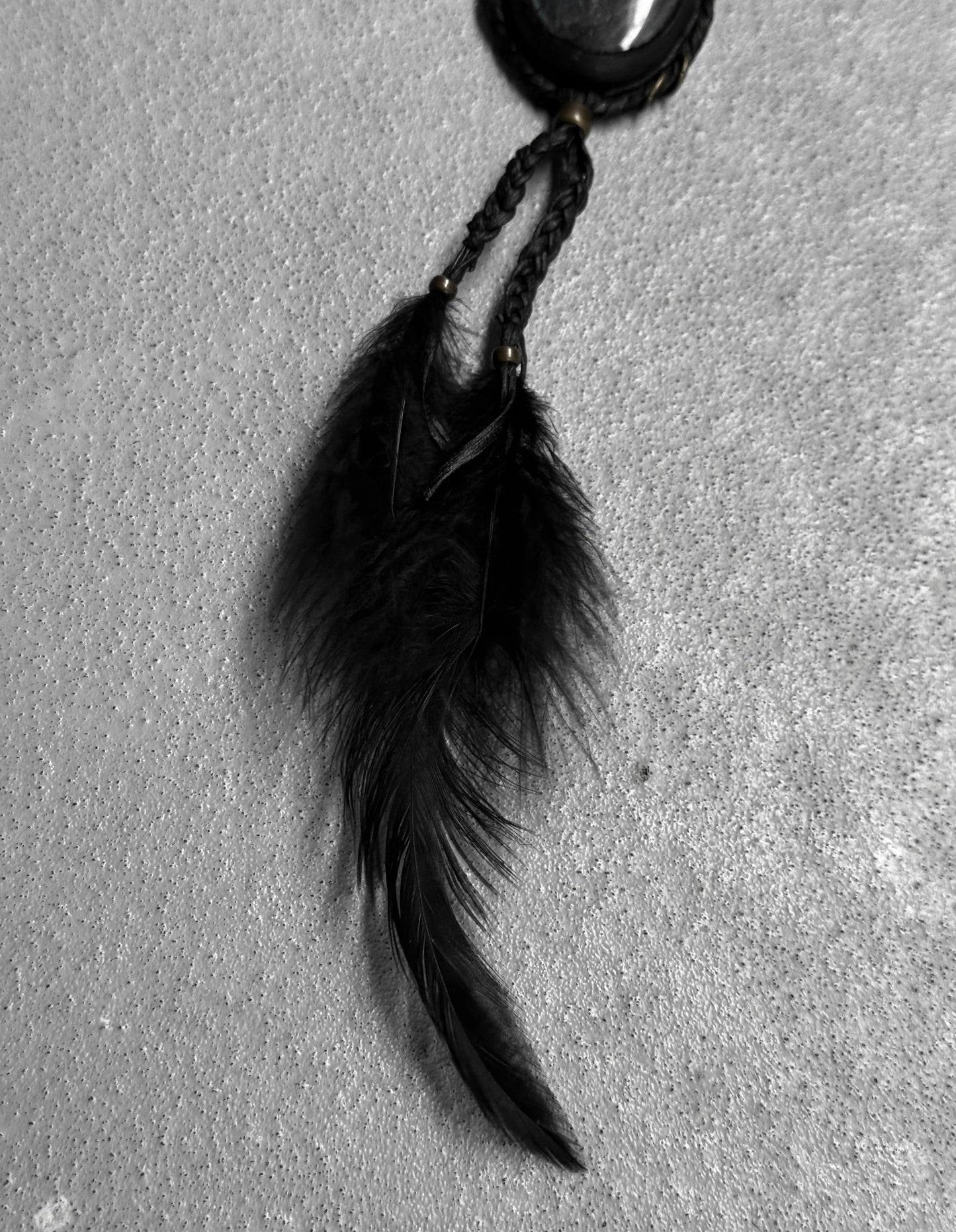 Black feathered keychain on a textured gray surface