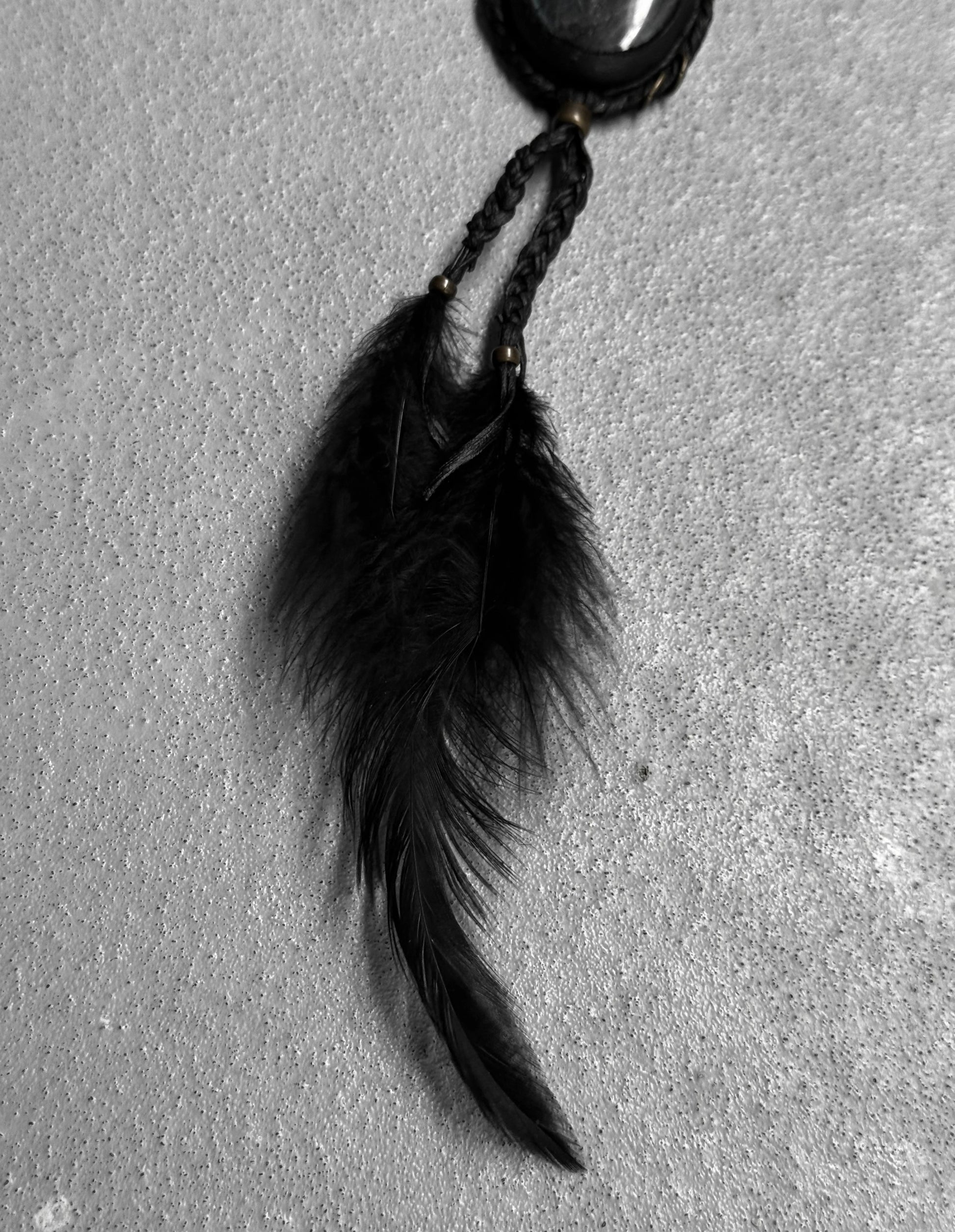 Black feathered keychain on a textured gray surface
