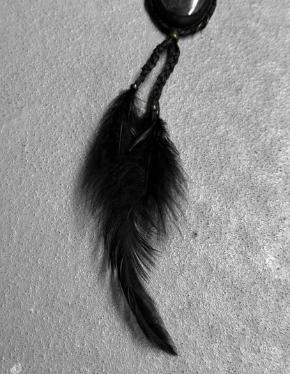 Black feathered keychain on a textured gray surface