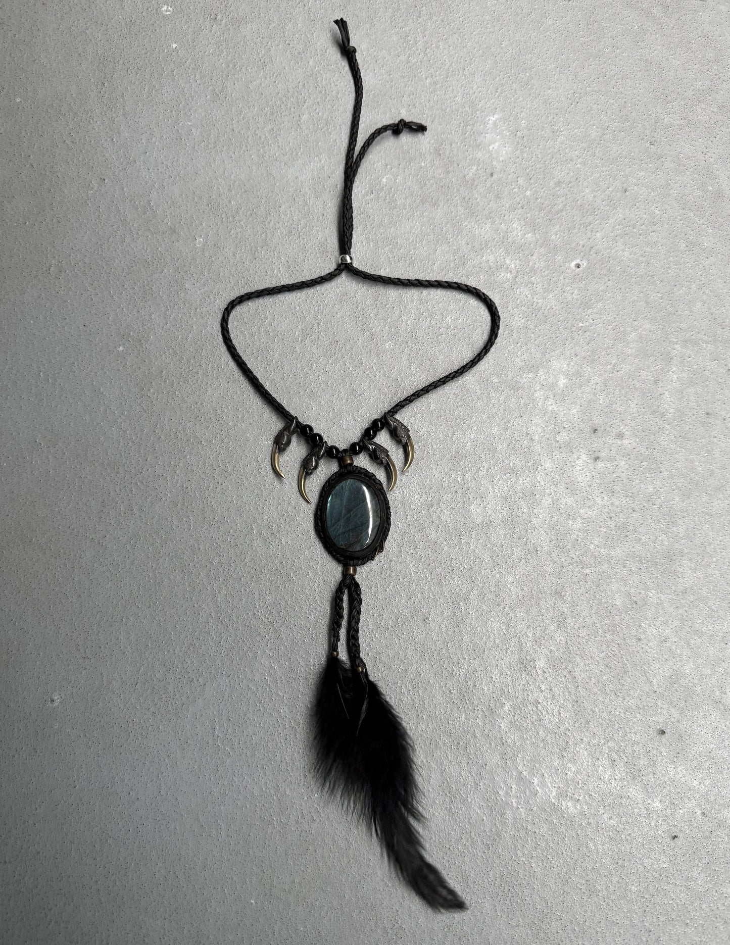 Black necklace with feather and stone pendant on a gray background