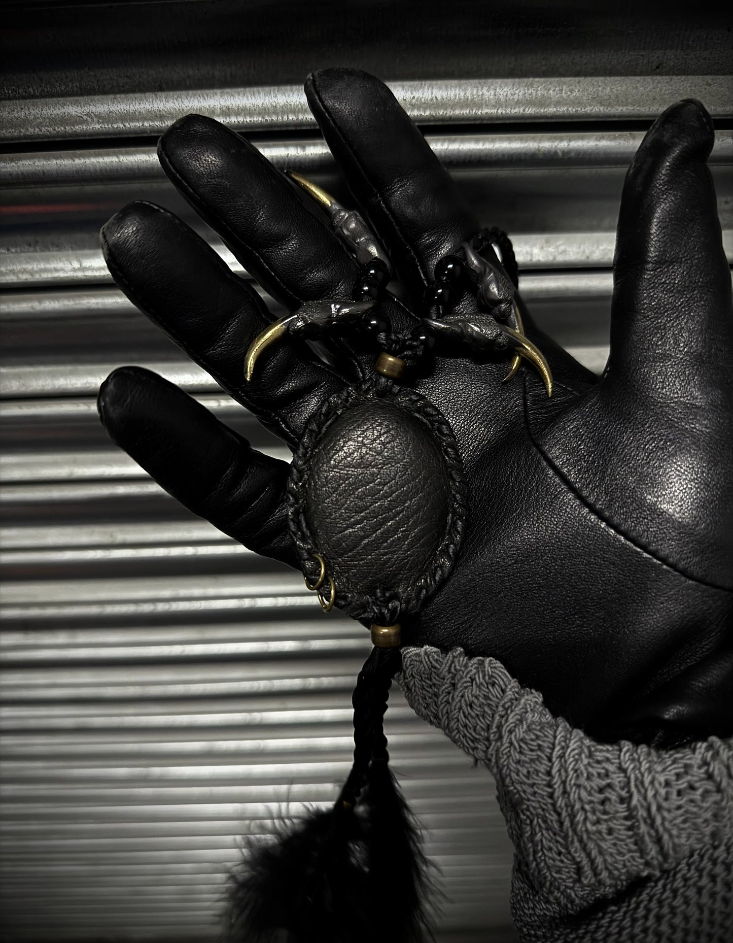 Black leather glove holding a black ball with gold chain against a metallic background