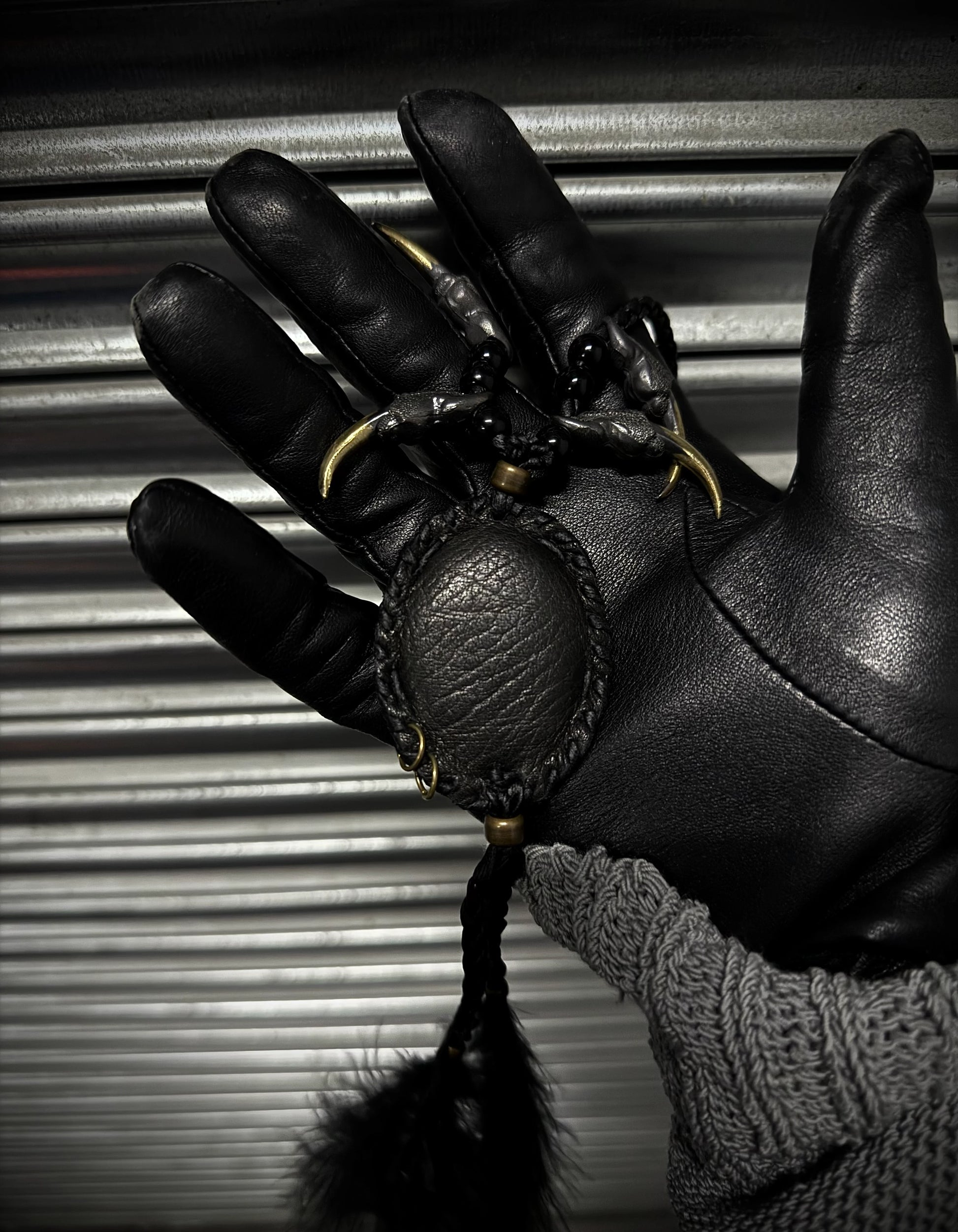 Black leather glove holding a black ball with gold chain against a metallic background