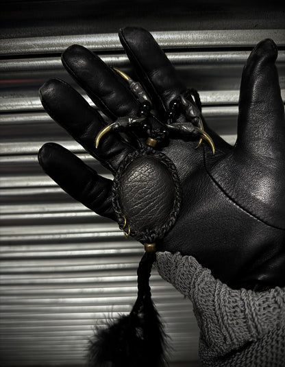 Black leather glove holding a black ball with gold chain against a metallic background
