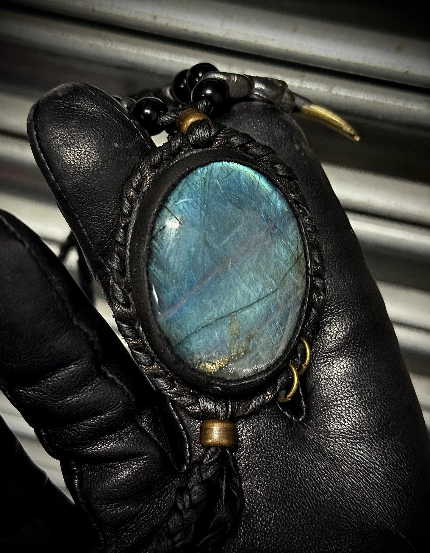 Leather-bound pendant with a blue stone held by a gloved hand against a metallic background
