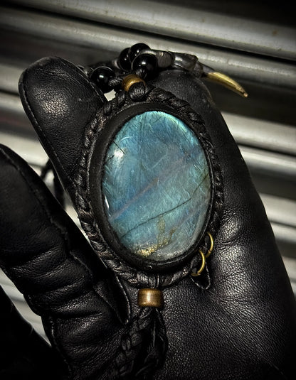 Leather-bound pendant with a blue stone held by a gloved hand against a metallic background