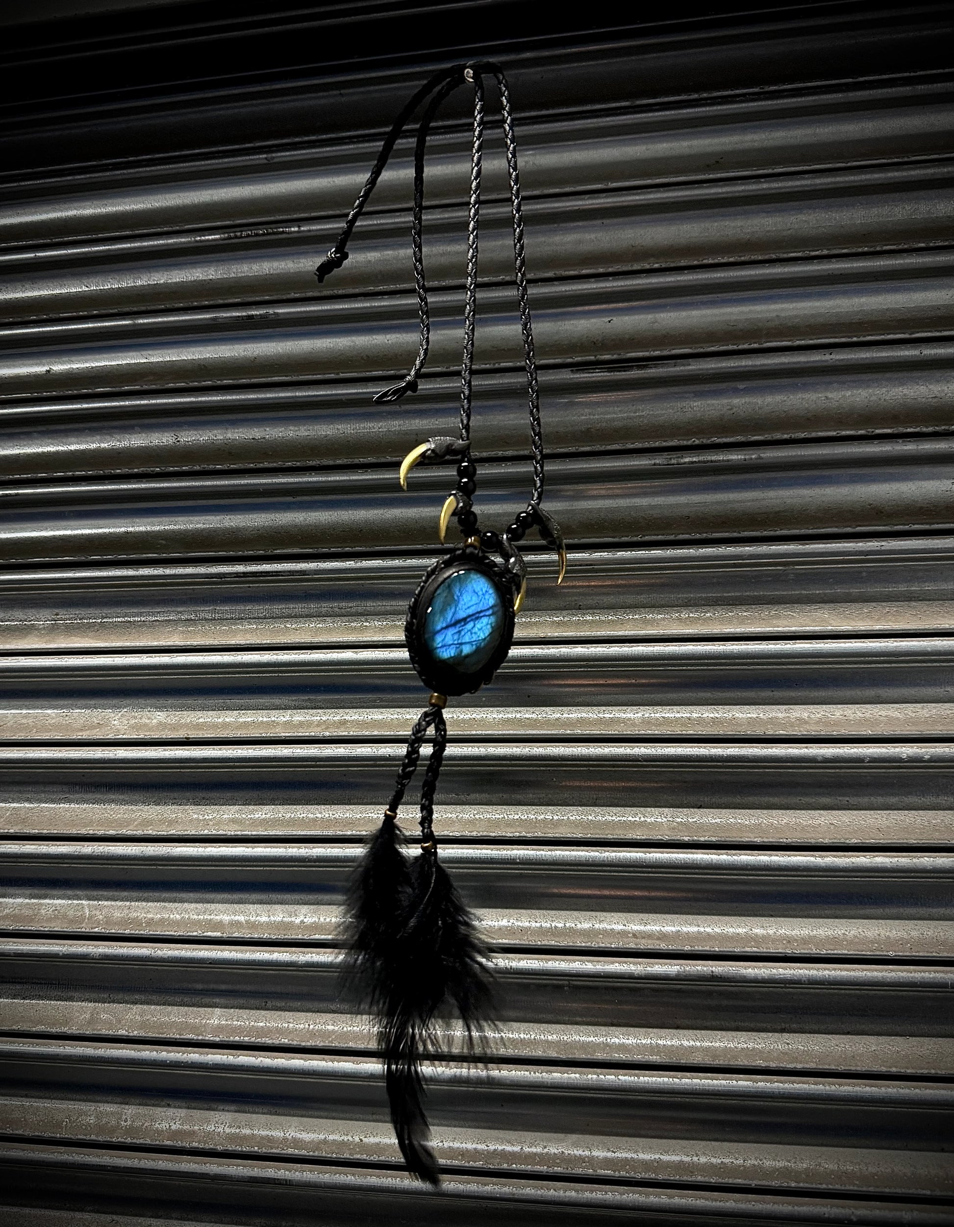 Decorative hanging item with a blue stone and feathers against a corrugated metal background