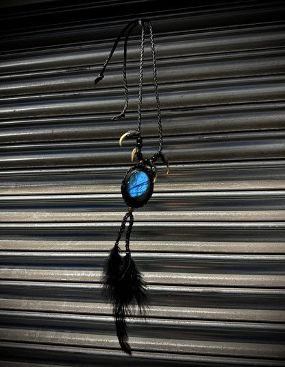 Decorative hanging item with a blue stone and feathers against a corrugated metal background