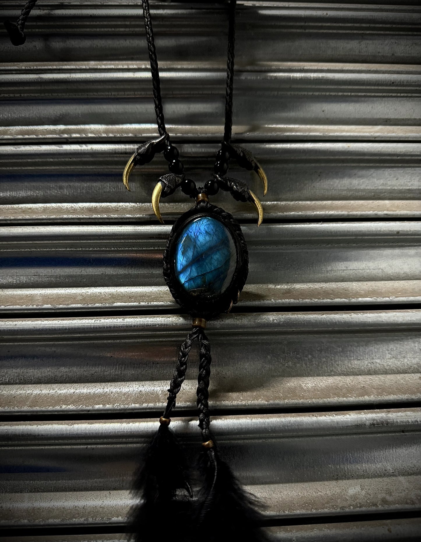 Necklace with blue stone and black feathers hanging against a corrugated metal background