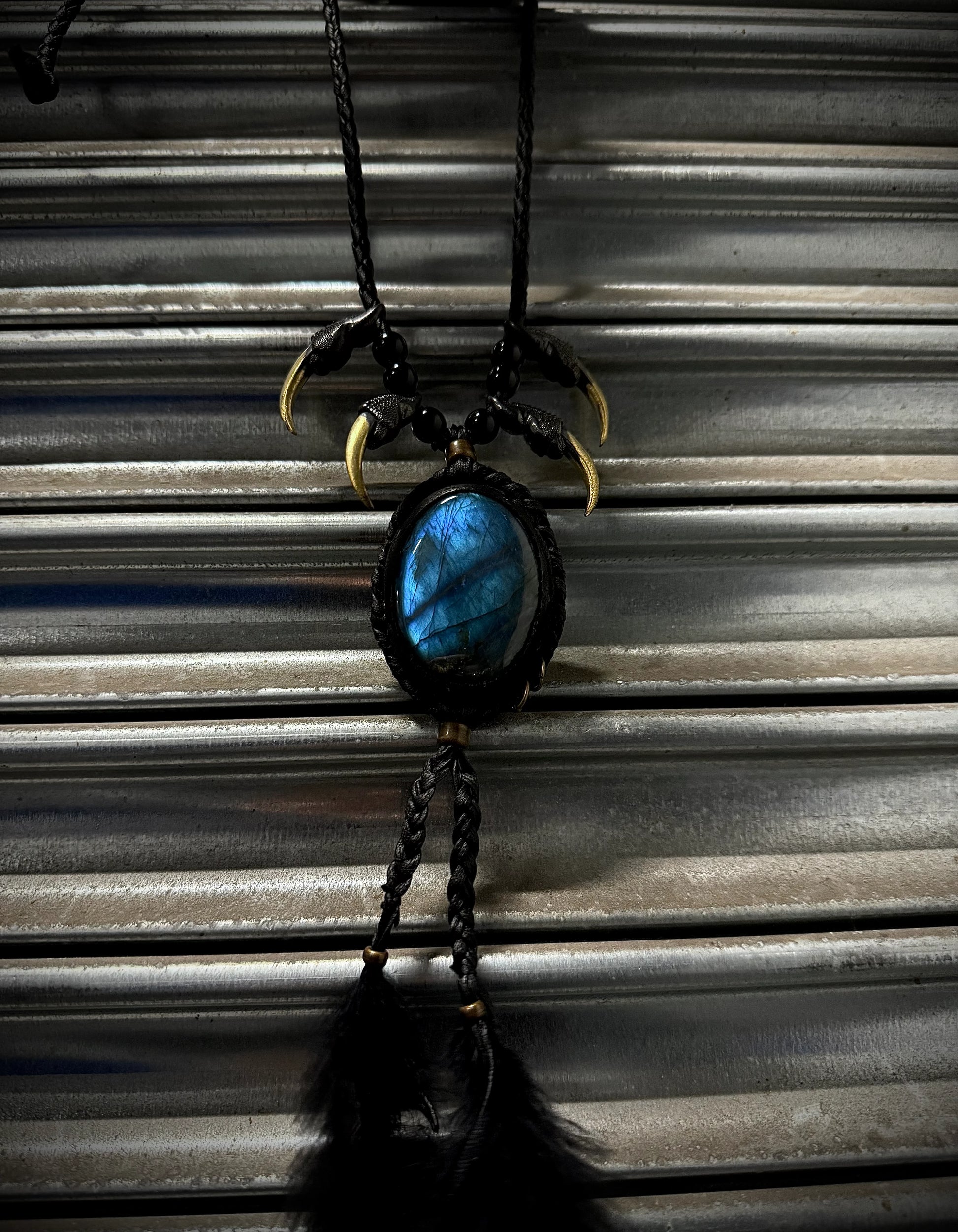 Necklace with blue stone and black feathers hanging against a corrugated metal background