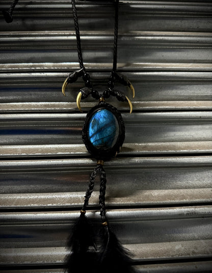 Necklace with blue stone and black feathers hanging against a corrugated metal background