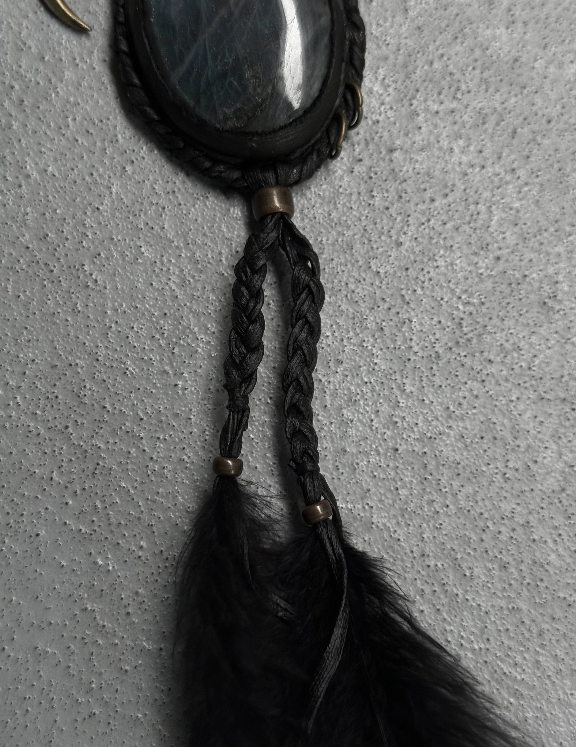 Black feathered keychain with braided design on a textured gray background