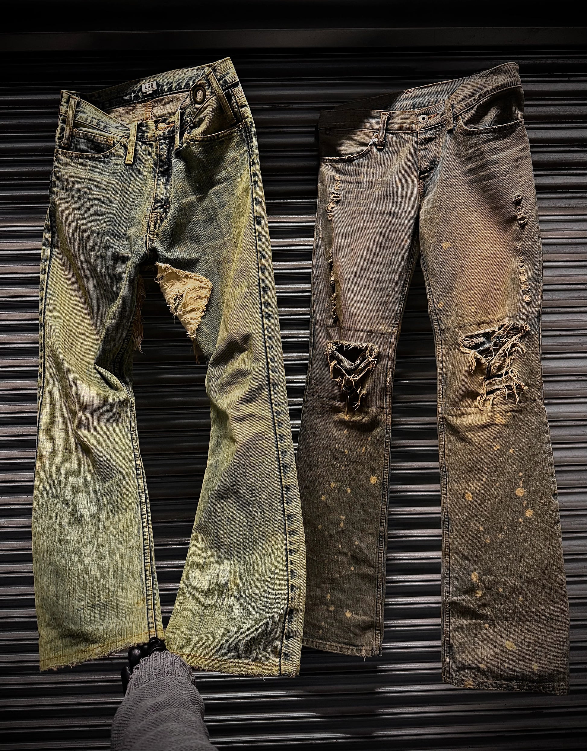 Two pairs of distressed jeans on a metallic surface
