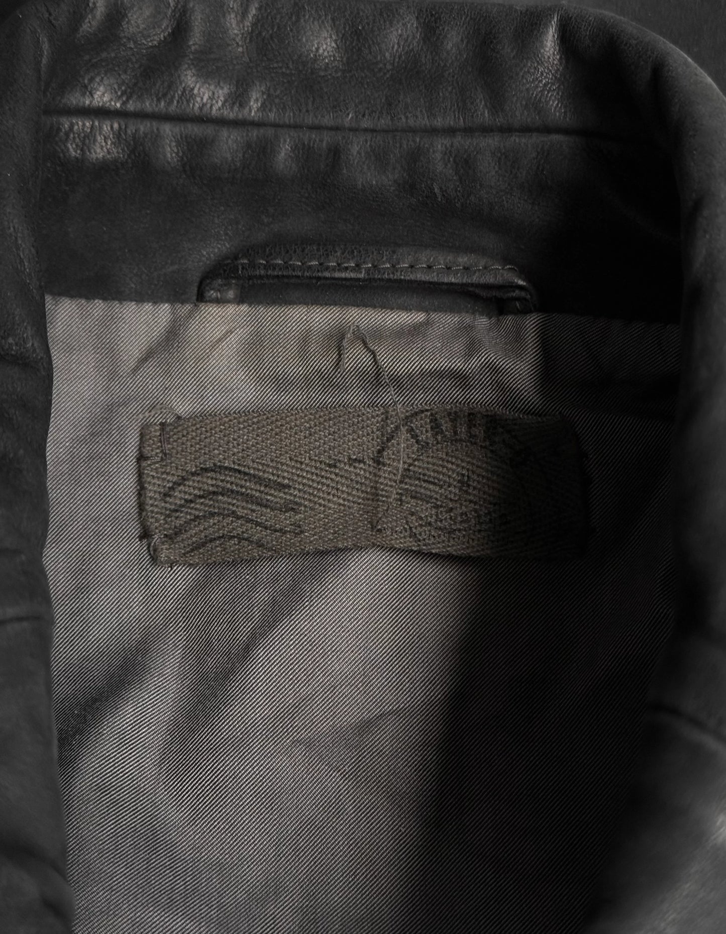 Close-up of a leather jacket with a brand logo on the chest pocket.