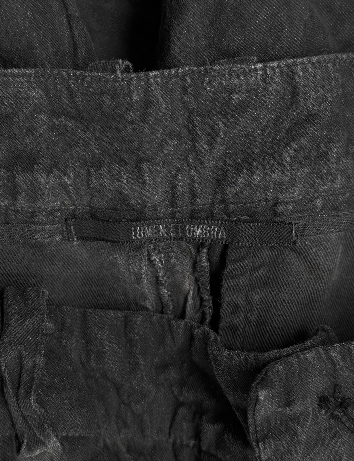 Close-up of a black denim jacket with 'Lumen et Umbra' branding on a dark background