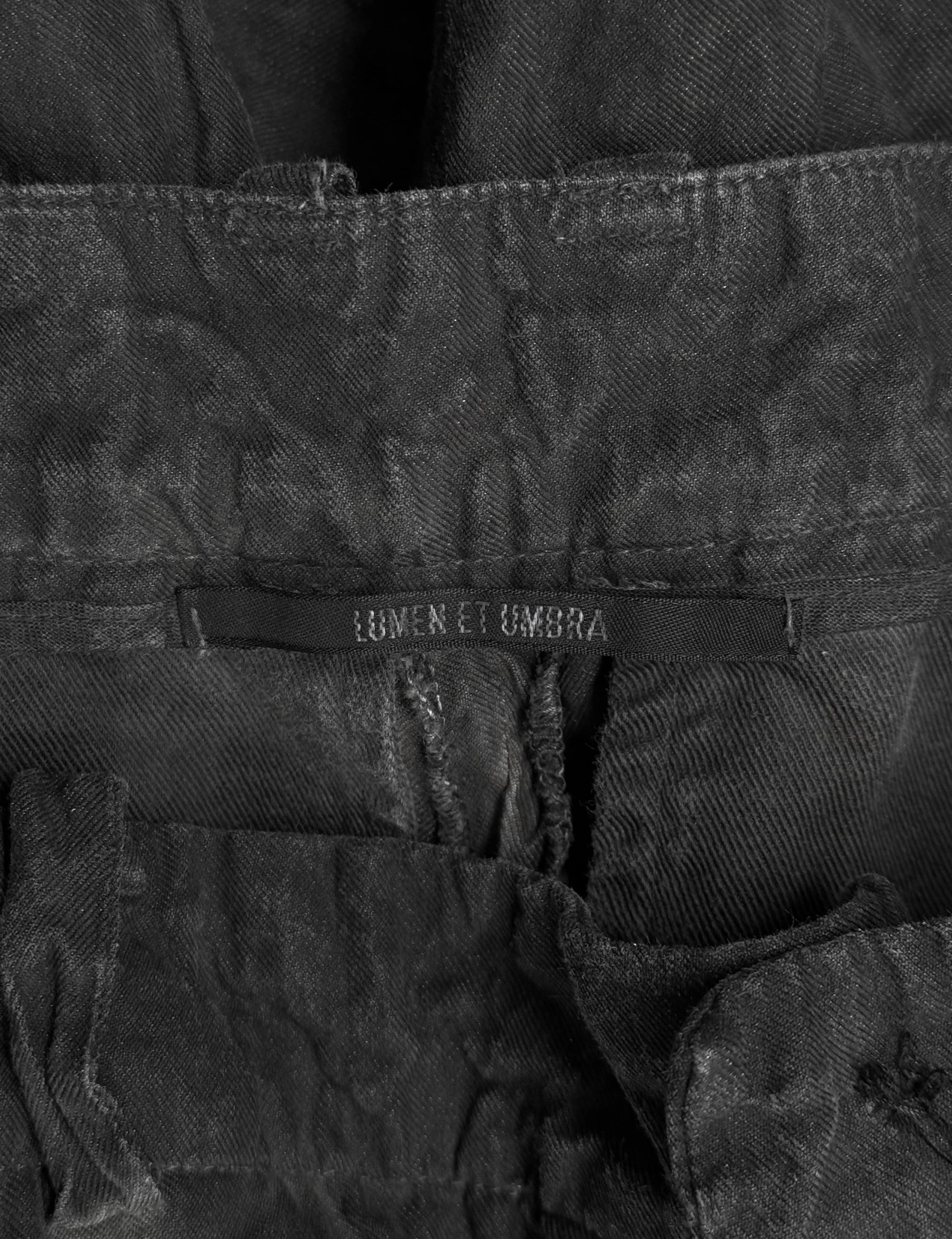 Close-up of a black denim jacket with 'Lumen et Umbra' branding on a dark background