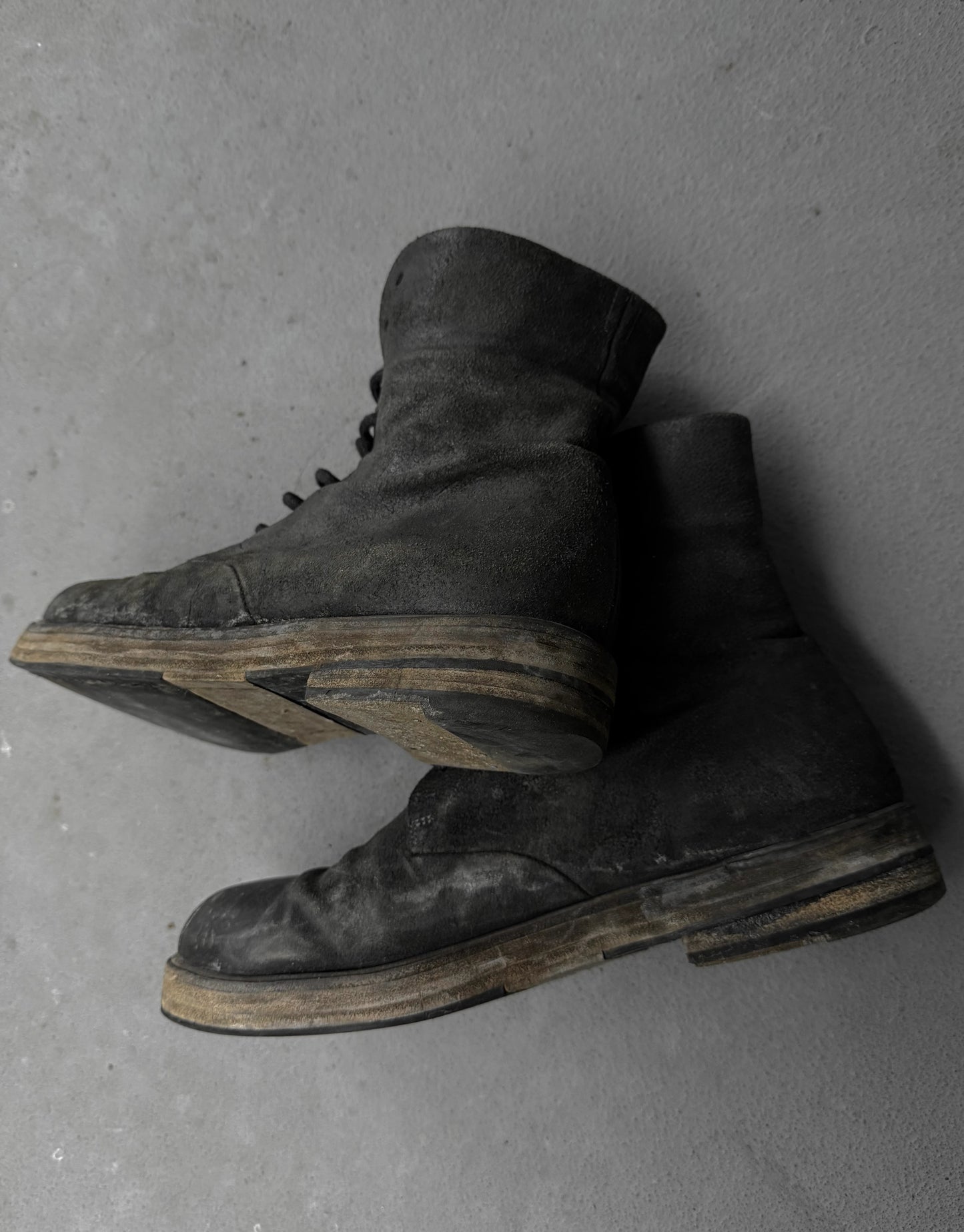Pair of worn black boots on a gray concrete floor