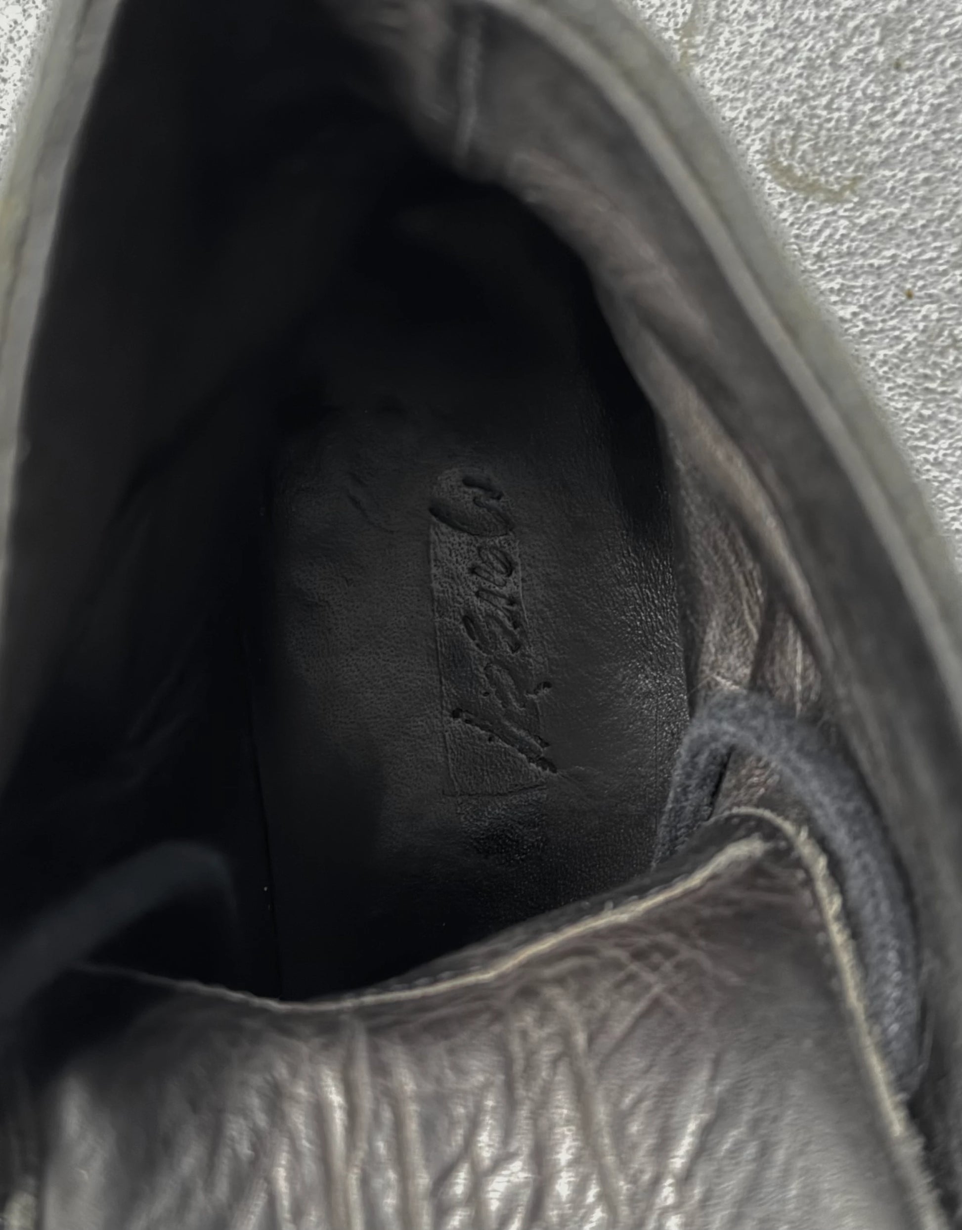 Close-up of a black leather shoe with visible stitching and brand logo.