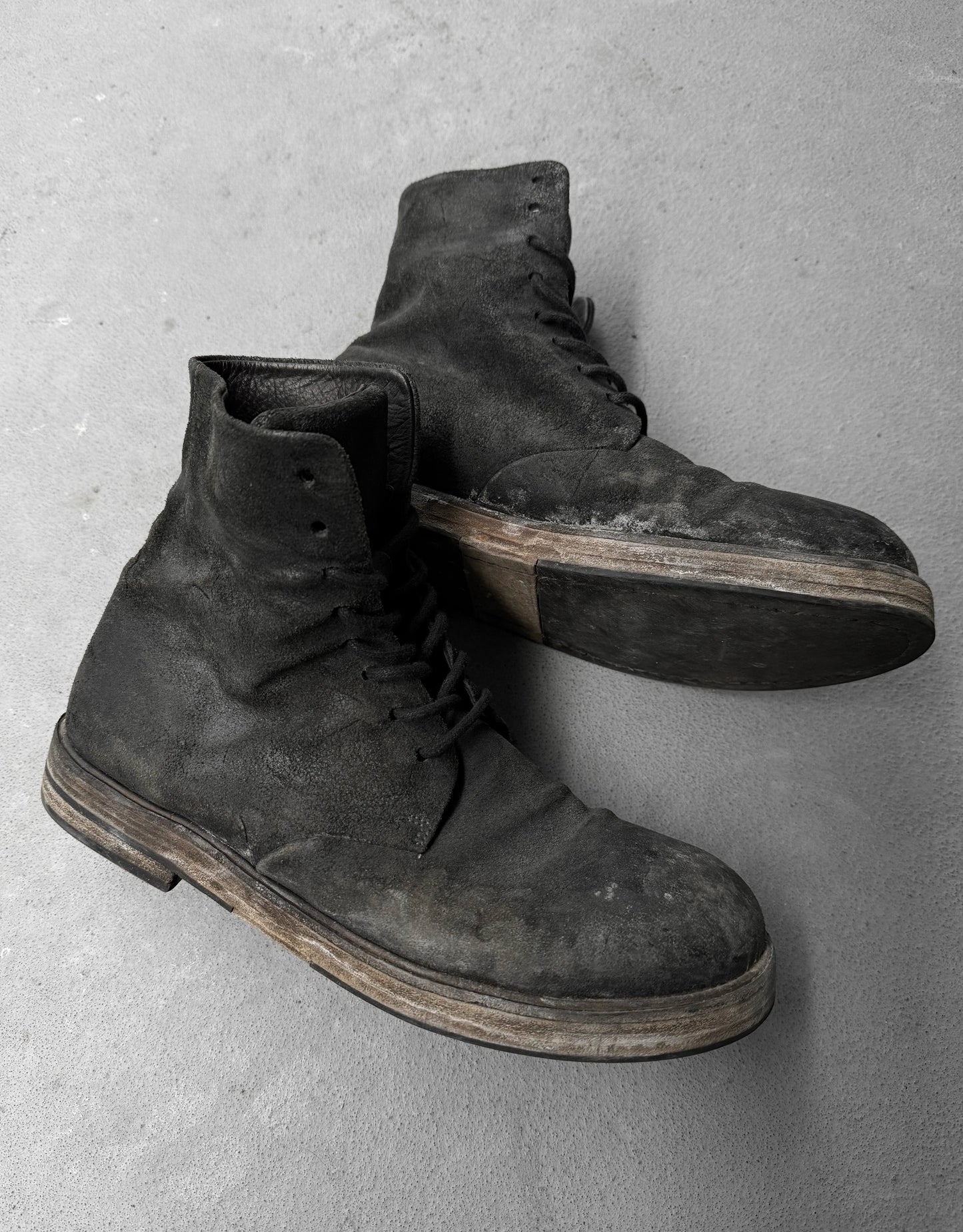 Pair of worn black boots on a gray concrete surface