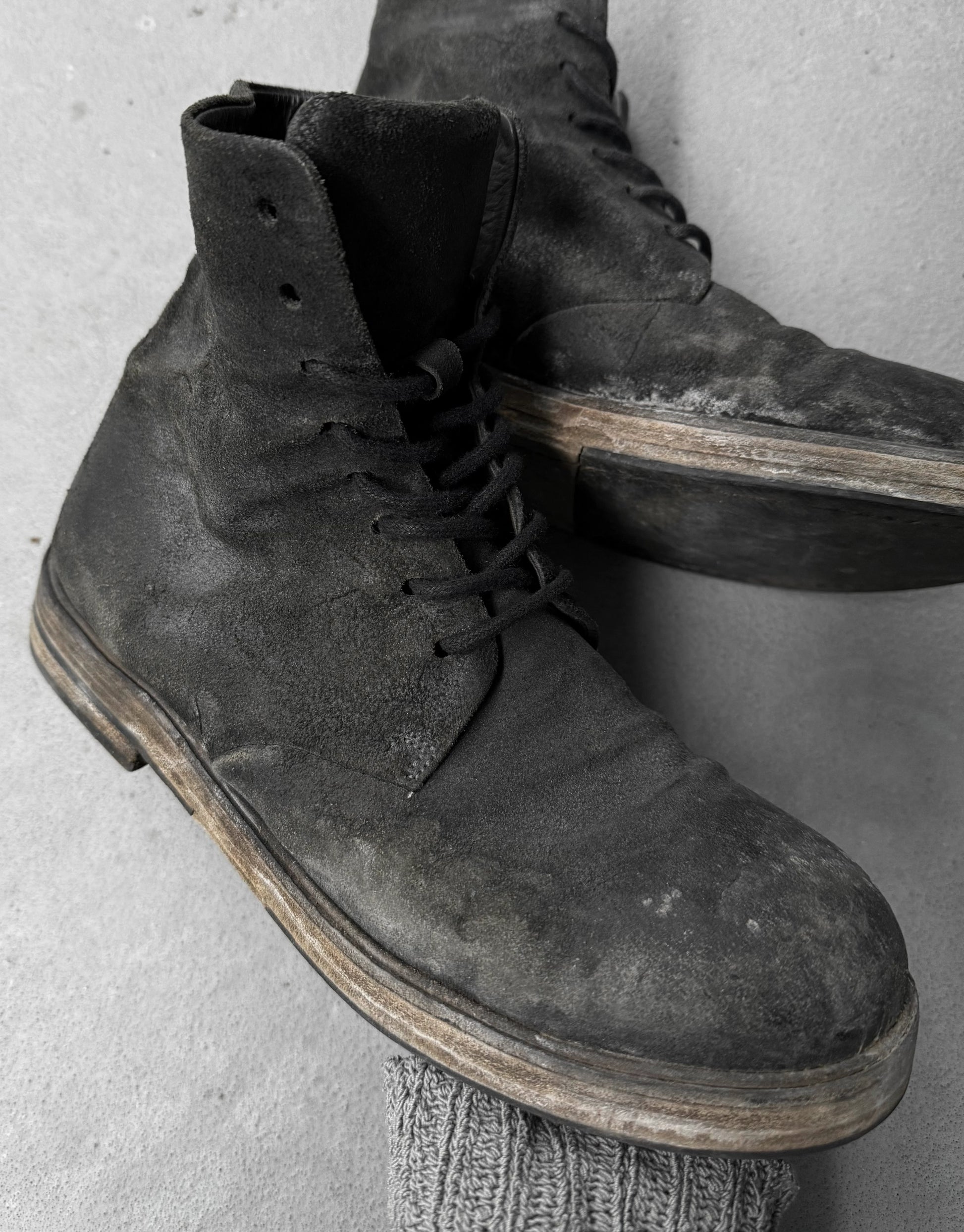 Pair of worn black leather boots on a light gray background