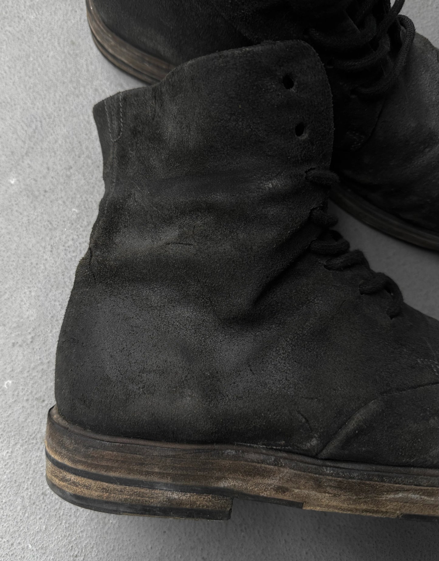 Close-up of black suede boots on a gray concrete surface