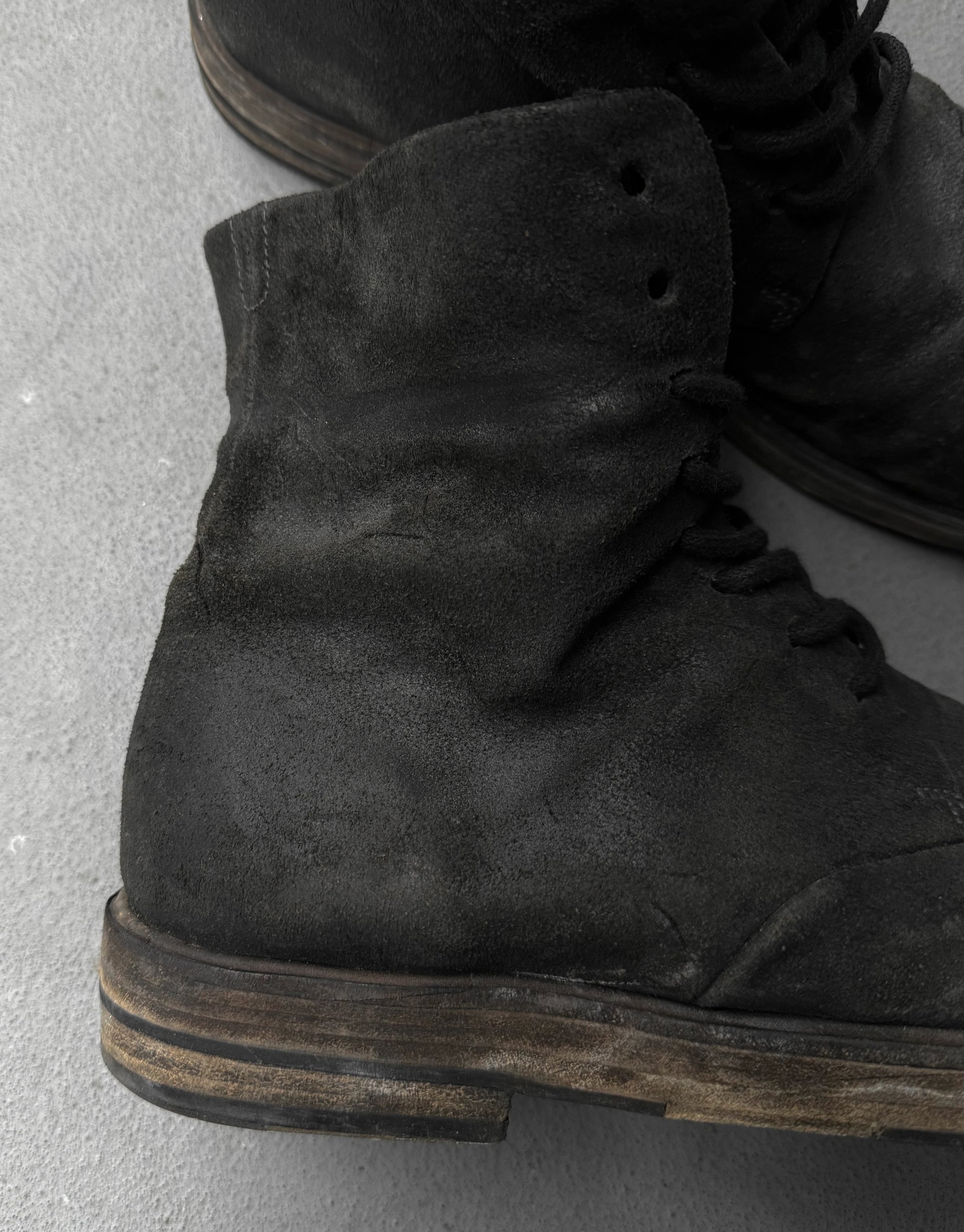 Close-up of black suede boots on a gray concrete surface
