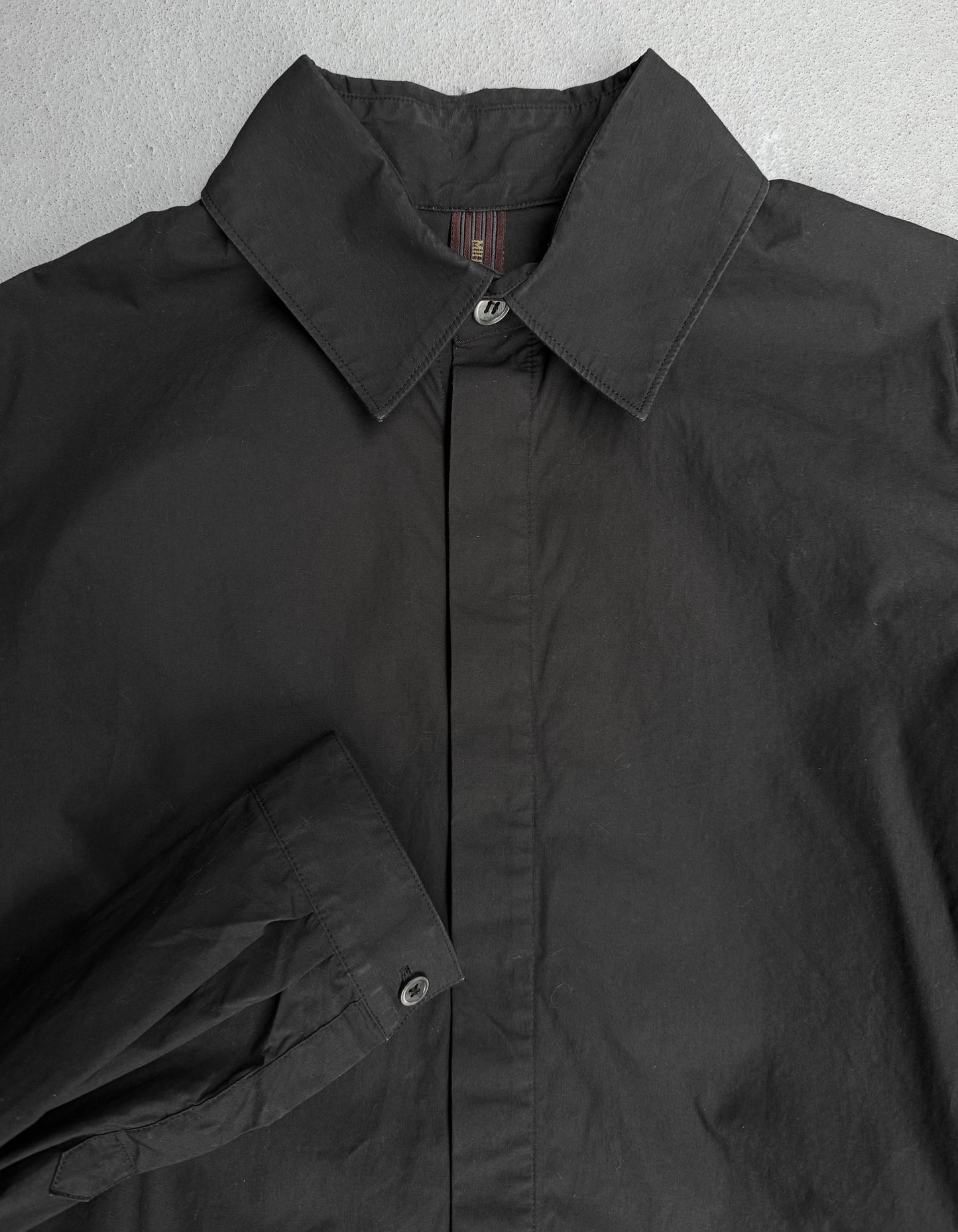 Close-up of a black jacket with a collar and button details on a gray background