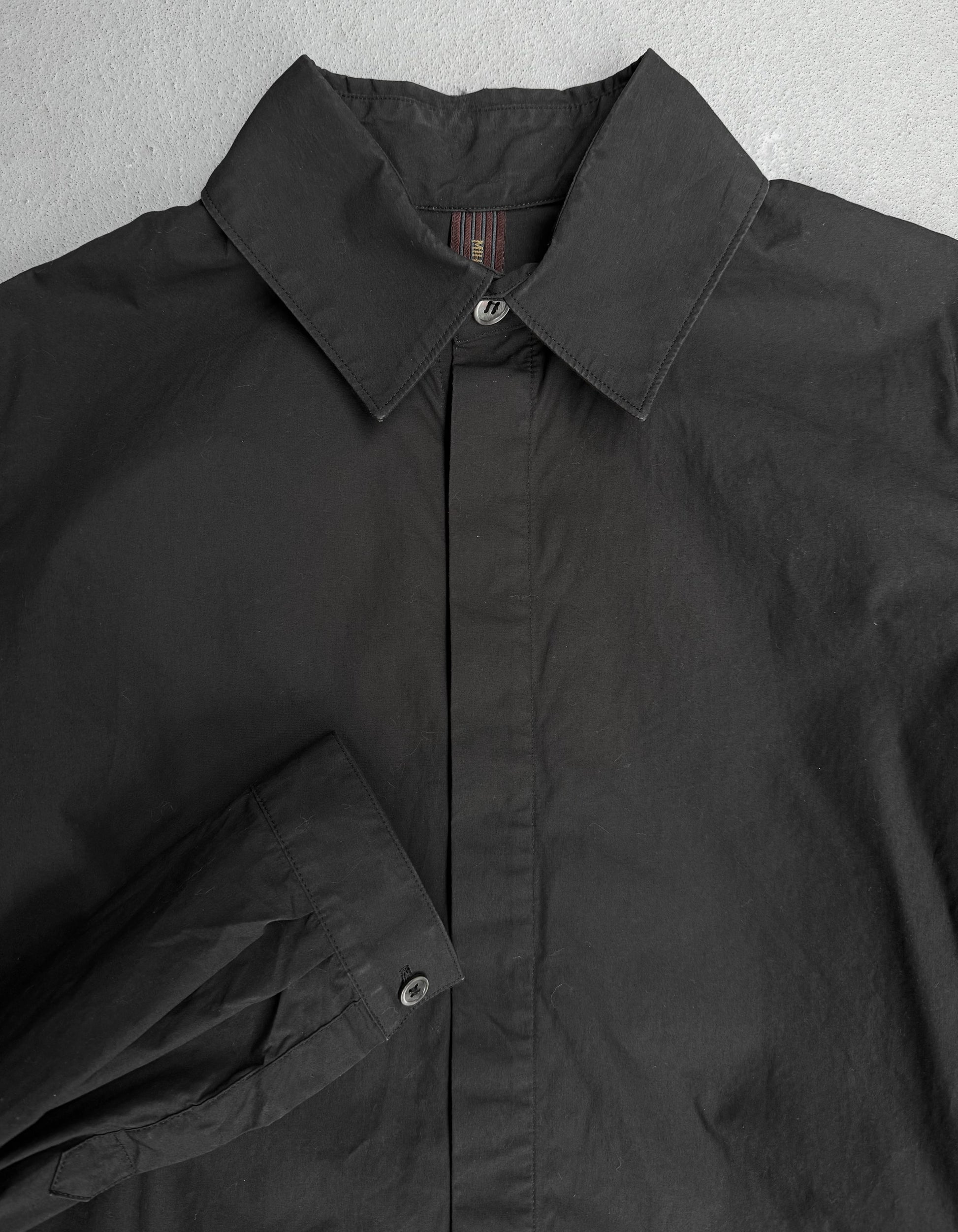 Close-up of a black jacket with a collar and button details on a gray background