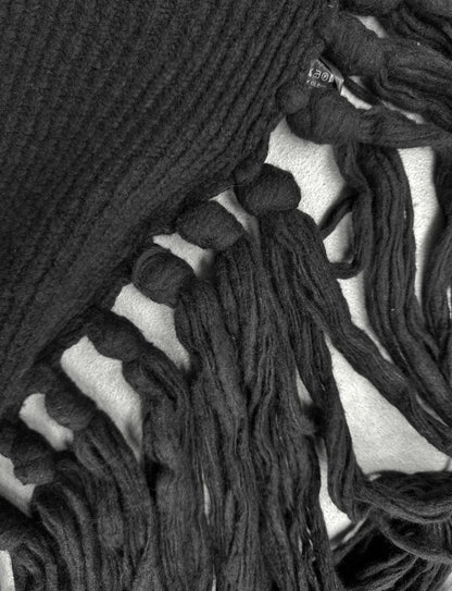Close-up of a black knitted scarf with tassels on a white background