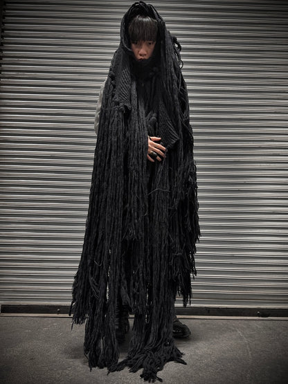 Person wearing a long, dark, textured coat in front of a metallic shutter.