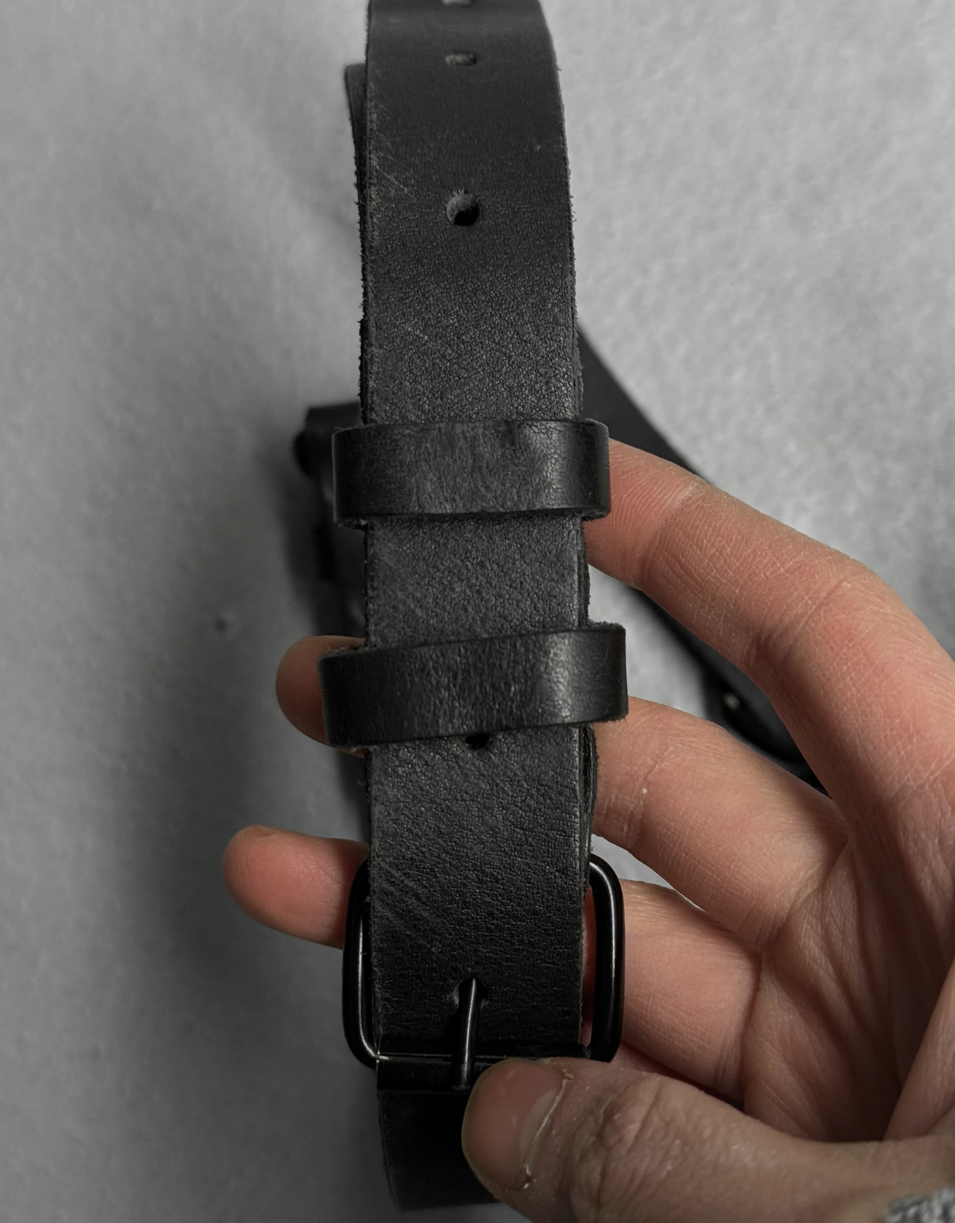 Black leather belt held by a hand against a gray background