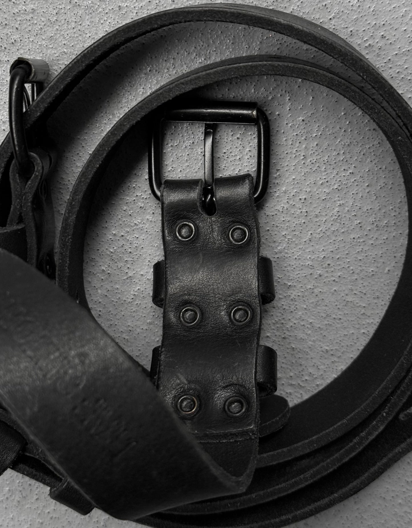 Close-up of a black leather belt with a buckle on a light gray background