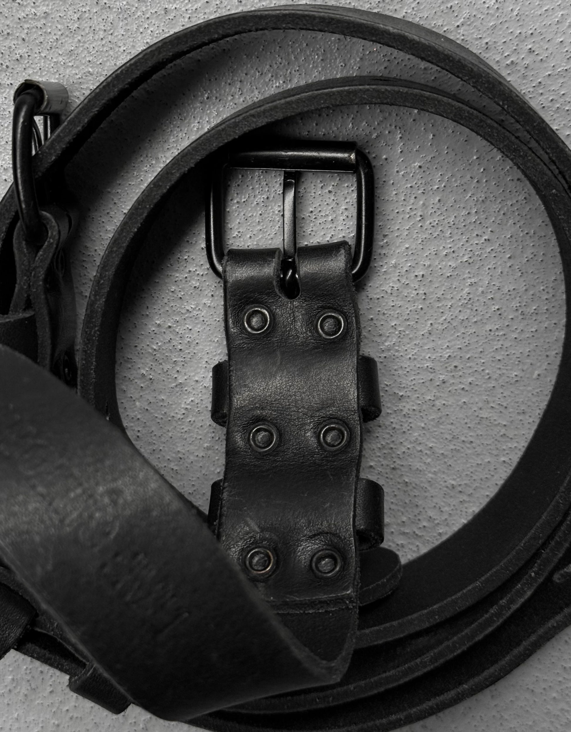 Close-up of a black leather belt with a buckle on a light gray background