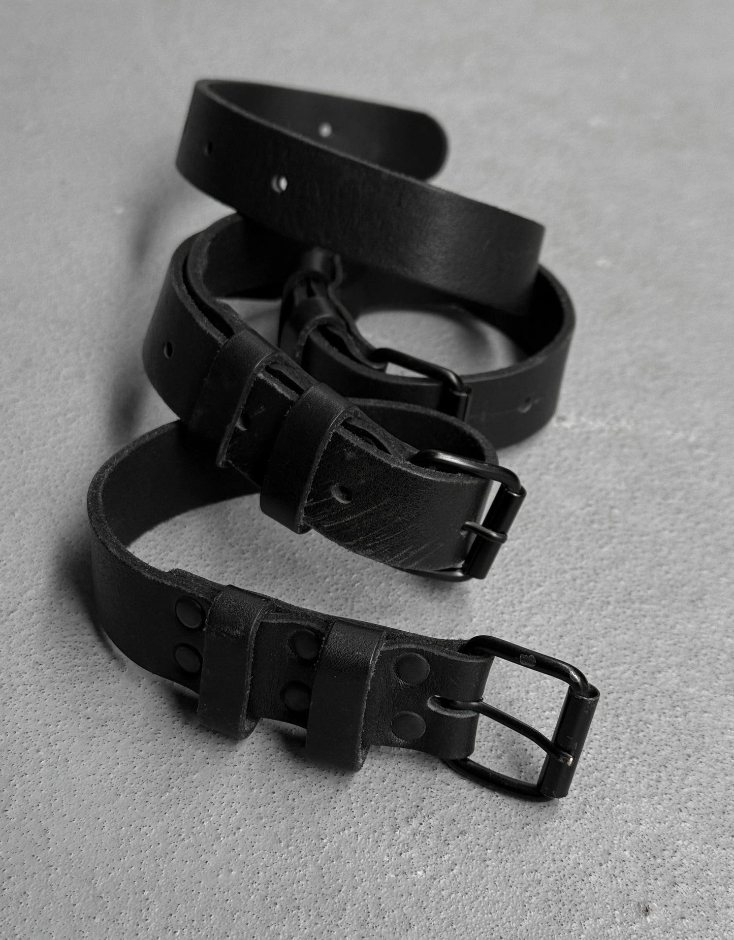 Three black leather belts arranged on a gray surface