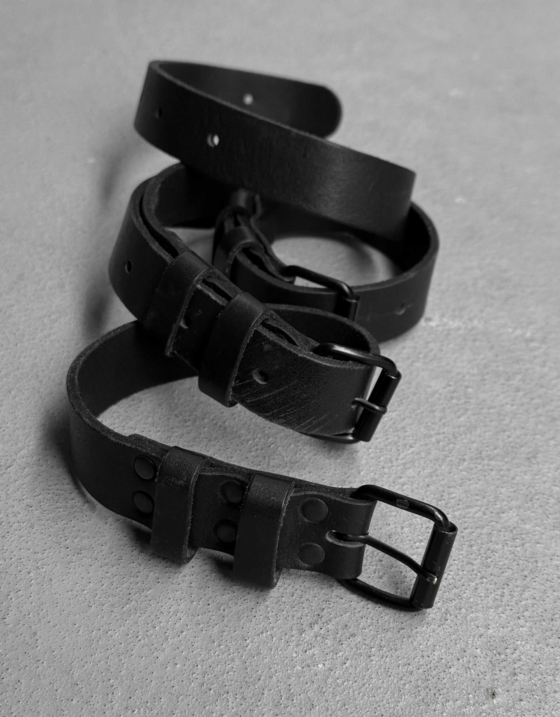 Three black leather belts arranged on a gray surface