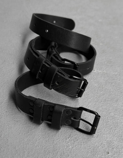 Three black leather belts arranged on a gray surface
