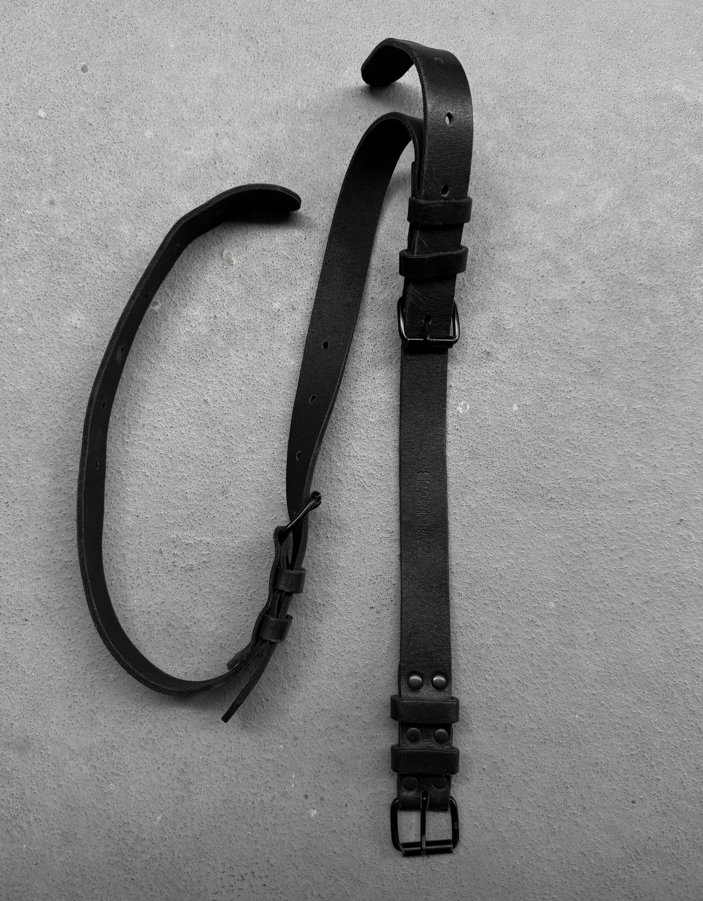Two black leather straps with buckles on a gray surface