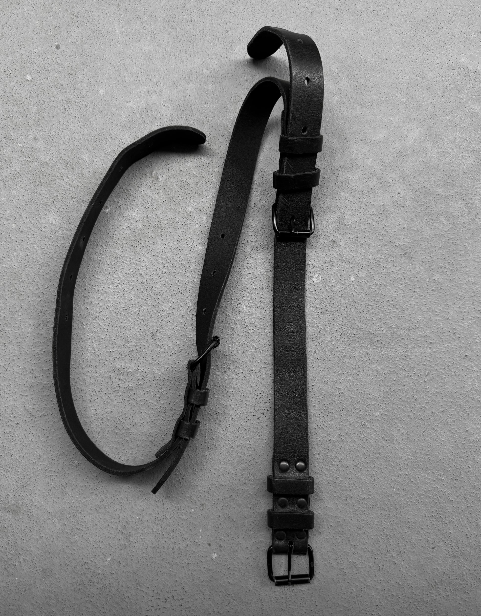Two black leather straps with buckles on a gray surface
