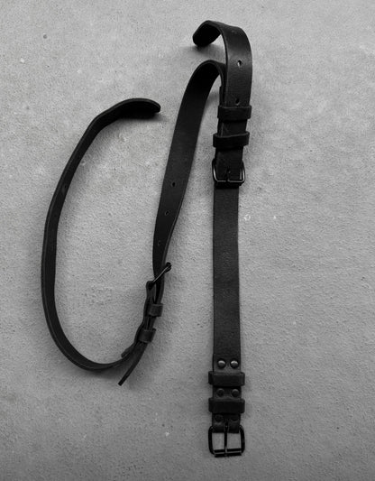 Two black leather straps with buckles on a gray surface