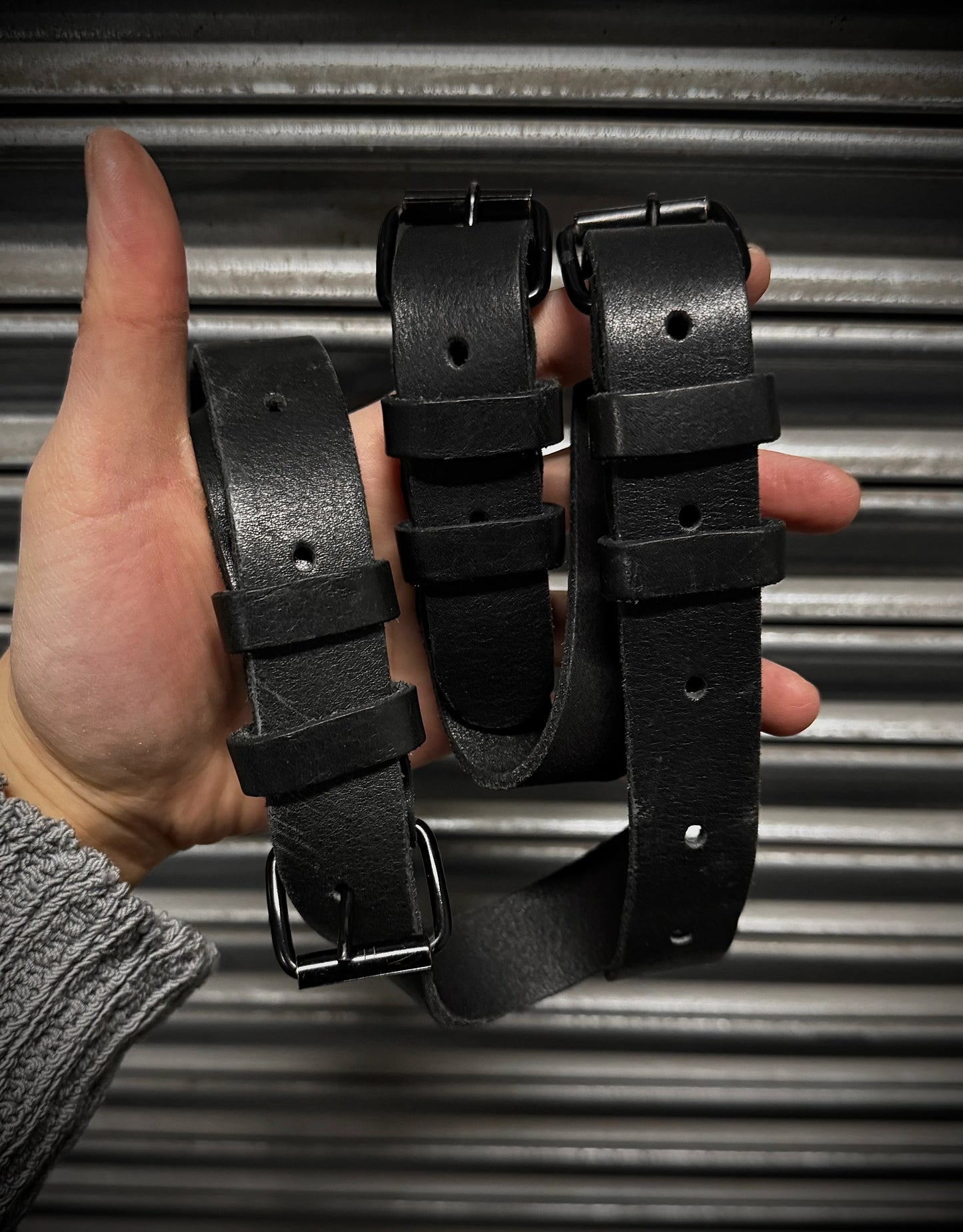 Three black leather belts held in a hand against a metallic background
