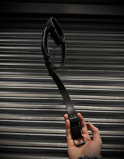 Black leather belt held by a hand against a metallic background