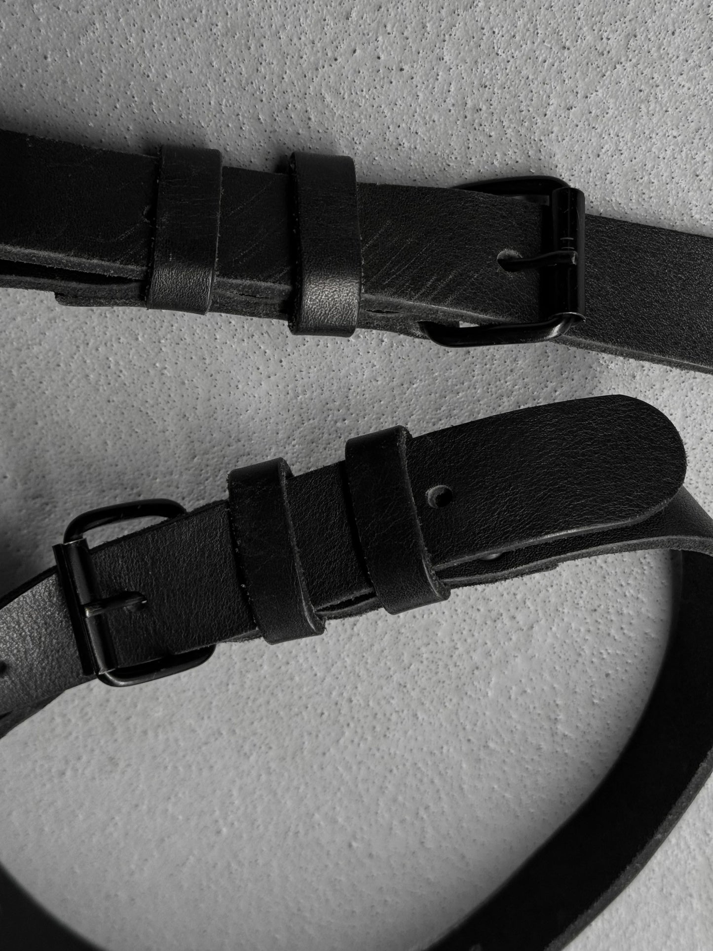 Two black leather belts with buckles on a light gray background