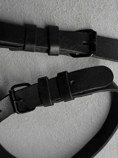Two black leather belts with buckles on a light gray background