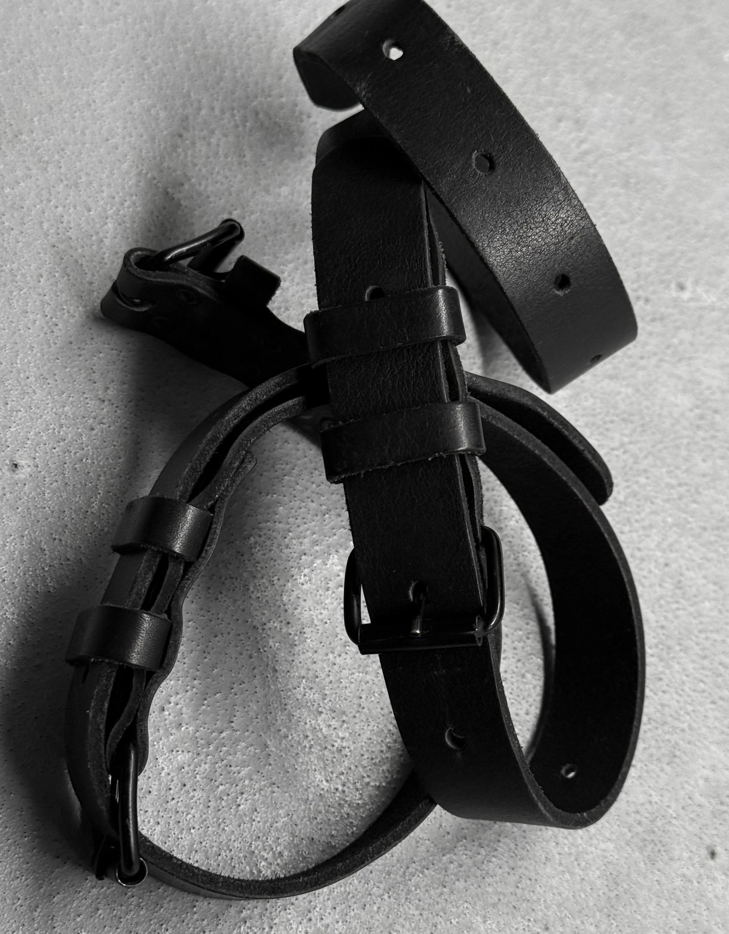 Black leather belt and strap on a textured gray surface