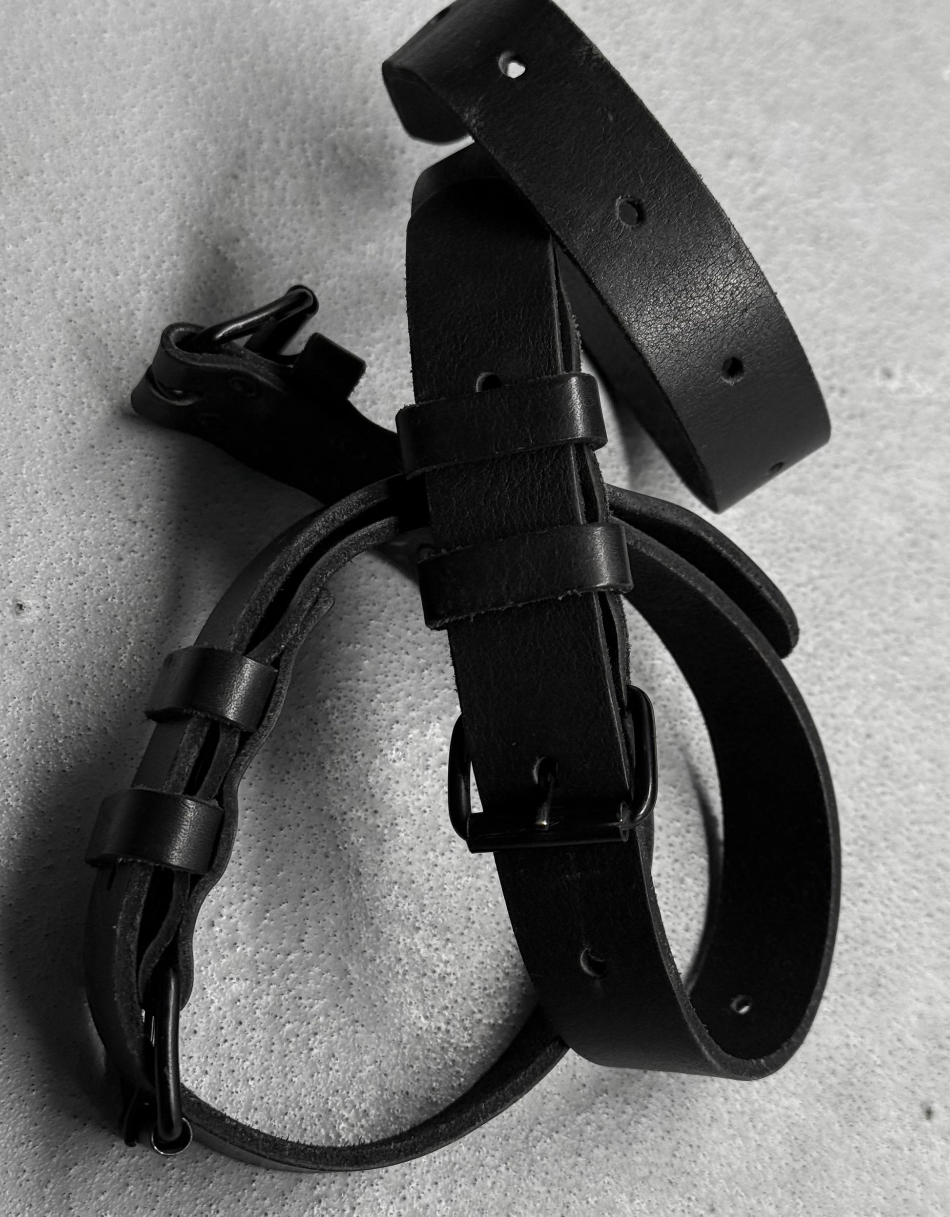 Black leather belt and strap on a textured gray surface